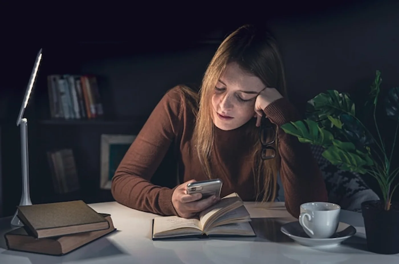 Estudante lendo um livro à noite, sozinha, ao lado de uma luminária